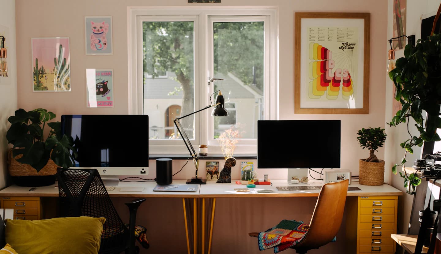 Deux postes de travail côte à côte sous une fenêtre, dans un bureau lumineux.